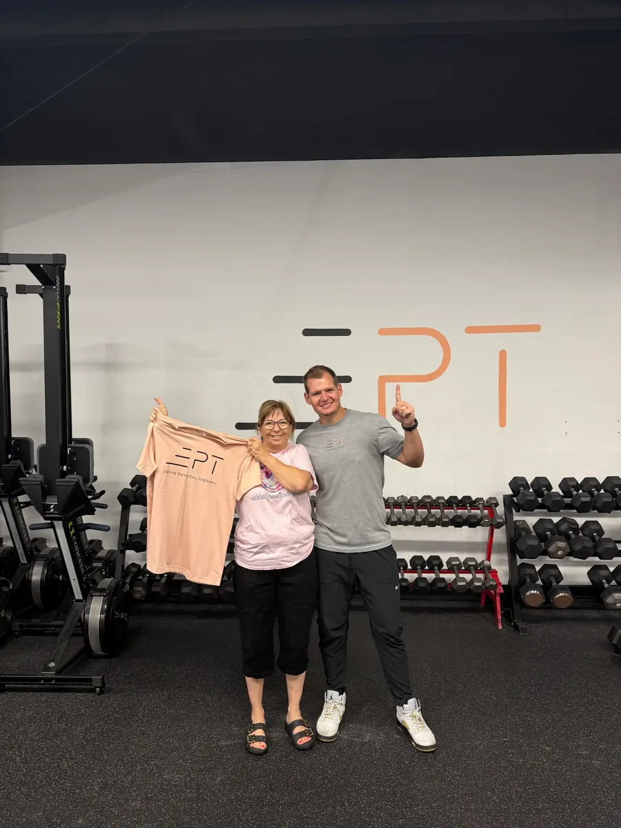 Patient holding a pink EPT shirt with their therapist in the clinic gym