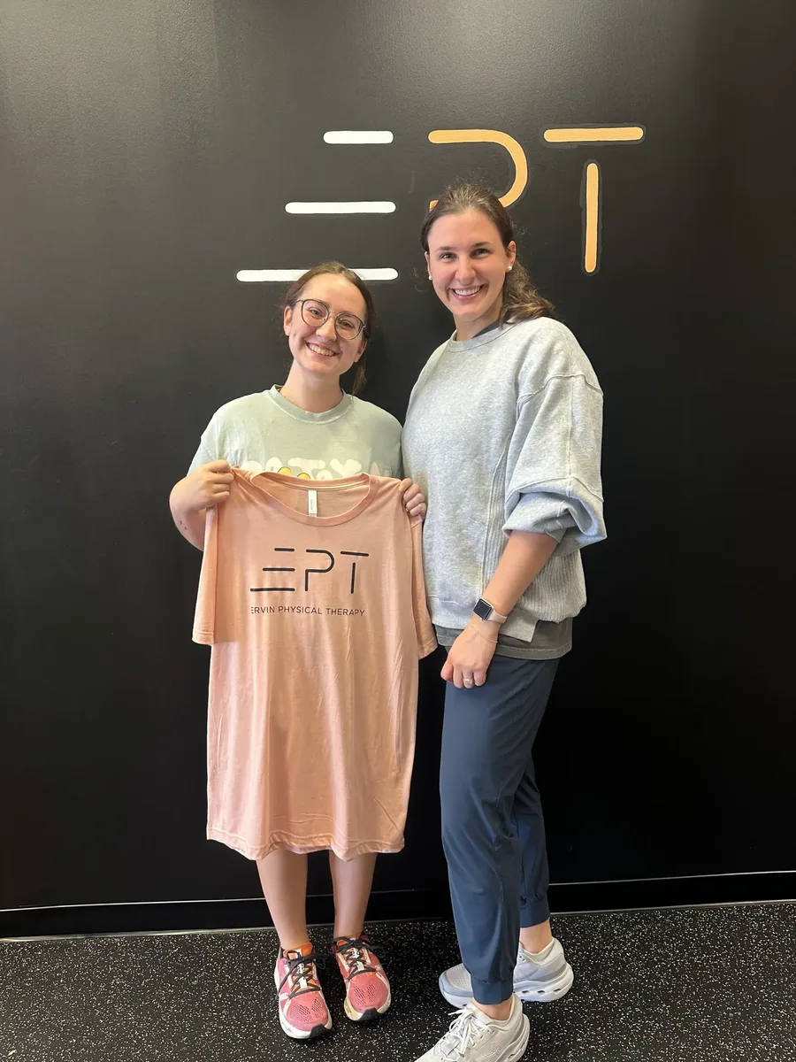 Young patient holding a pink EPT shirt beside their therapist