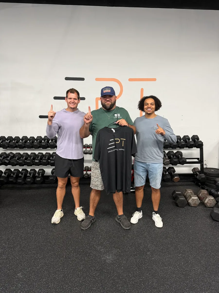 Three patients in the clinic gym, one holding a black EPT shirt