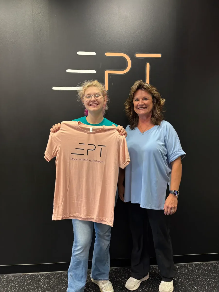 Patient holding up a pink EPT shirt next to their therapist