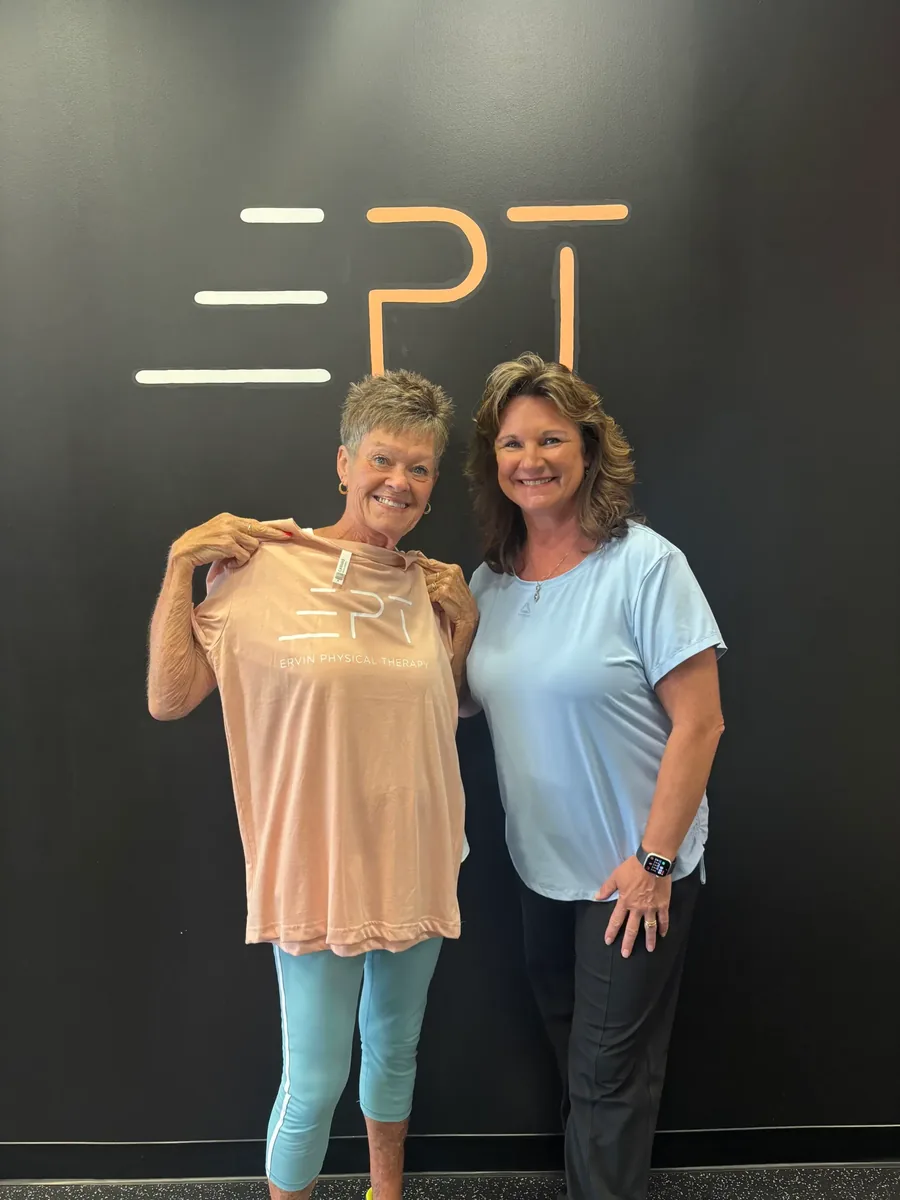 Smiling patient holding a pink EPT shirt beside their therapist