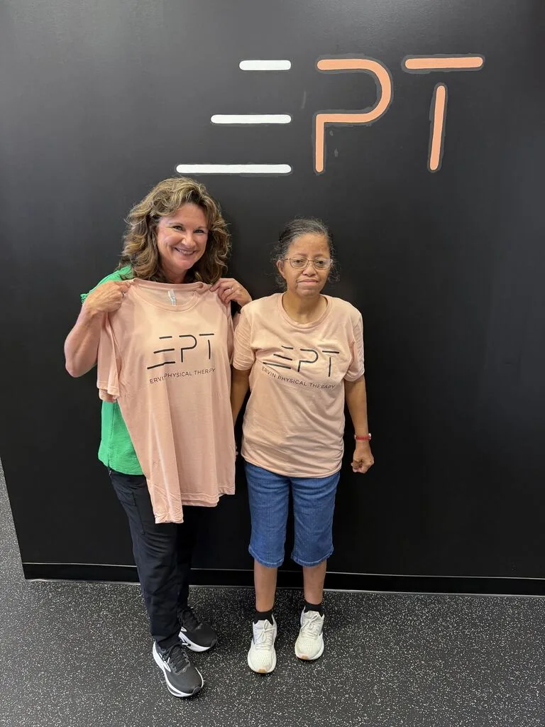 Two patients holding pink EPT shirts in front of the EPT logo wall