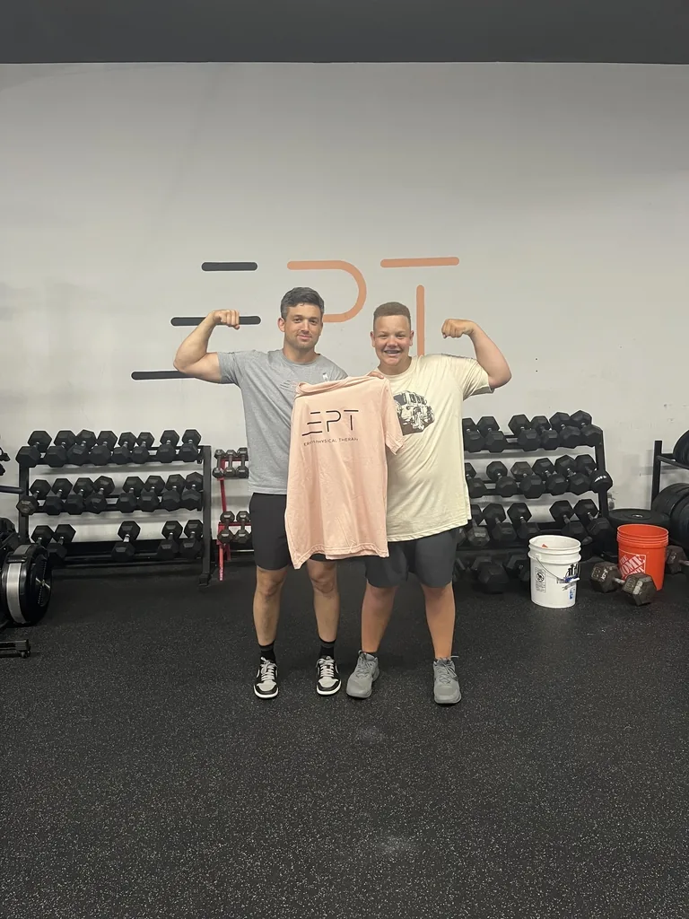 Patient holding a pink EPT shirt beside their therapist in the clinic gym